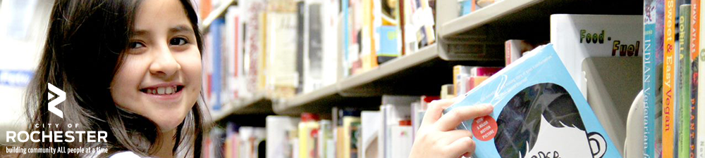 young girl pulling book off shelf while smiling at camera