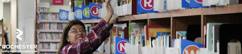 woman pulling book off shelf while smiling at camera