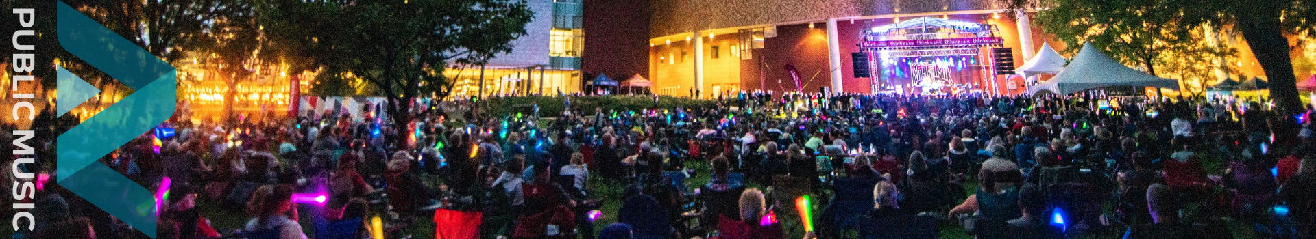 Banner of an evening concert with crowds of people watching the performers on stage.